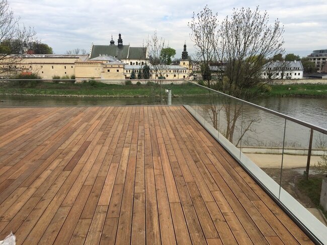 Długi taras drewniany na balkonie ze szklaną balustradą
