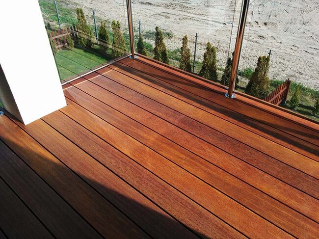 Balkon wykończony deskami z drewna egzotycznego ze szklaną balustradą .