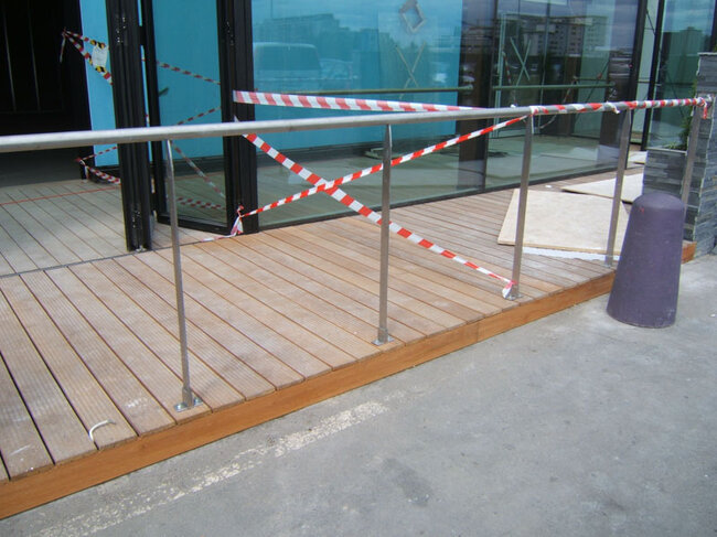 Drewniany podest wejściowy z balustradą ze stali nierdzewnej przy budynku .
