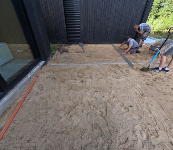 Przygotowanie podłoża patio pokazujące wyrównywanie gruntu piaskiem do instalacji płyt