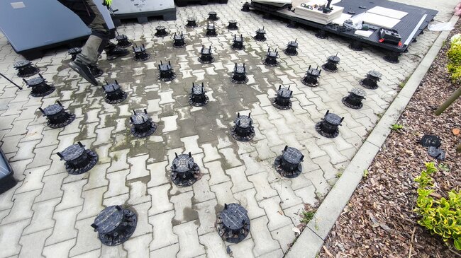 Układ siatki regulowanych plastikowych wsporników umieszczonych na kostce brukowej do montażu tarasu zewnętrznego