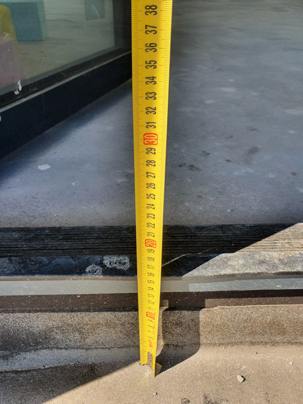Yellow measuring tape measuring the height of a doorway threshold or step.