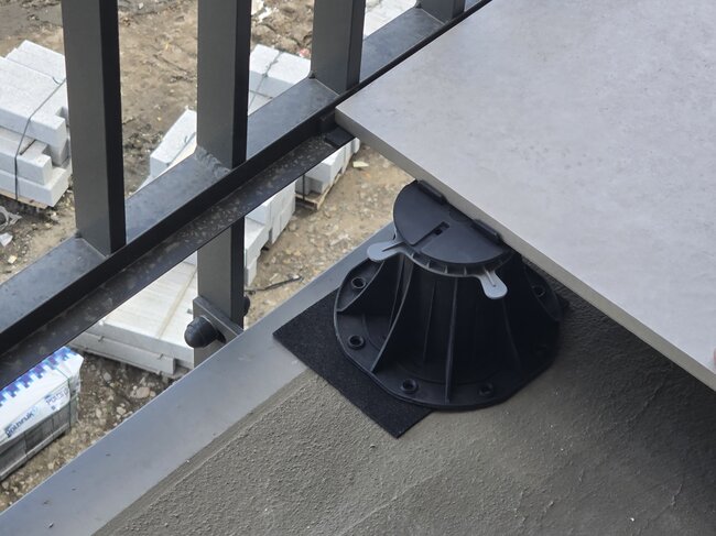 Regulowany plastikowy wspornik podtrzymujący płytkę porcelanową wzdłuż krawędzi balkonu.