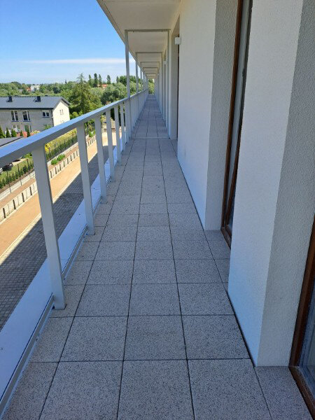 Ukończona długa zewnętrzna posadzka tarasowa z płytami tarasowymi o betonowej fakturze i białymi balustradami.