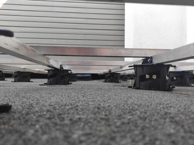 Widok z niskiej perspektywy na regulowane plastikowe wsporniki tarasowe podtrzymujące aluminiowe legary do tarasów wentylowanych.