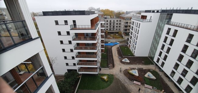 Widok z lotu ptaka pod wysokim kątem na nowoczesny kompleks mieszkalny z balkonami i zagospodarowanymi dziedzińcami.