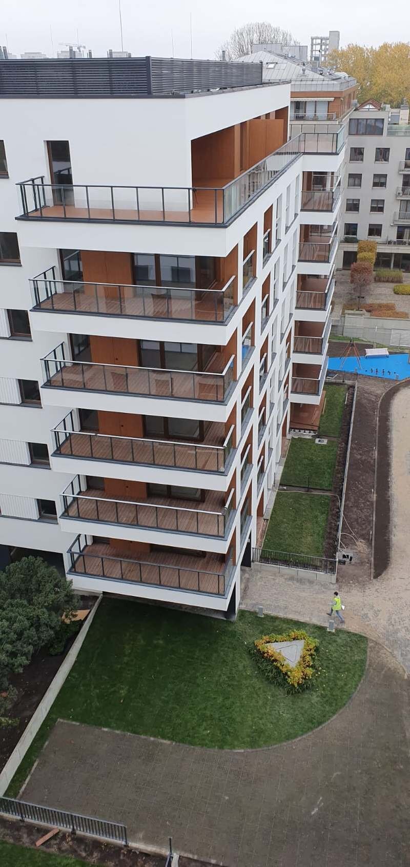 Widok z zewnątrz nowoczesnego wielokondygnacyjnego budynku mieszkalnego z balkonami wykończonymi drewnem i szklanymi balustradami.