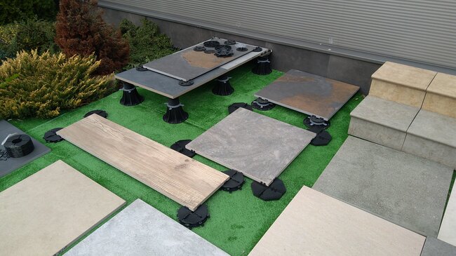 Outdoor display of adjustable pedestals supporting various patio pavers and decking.