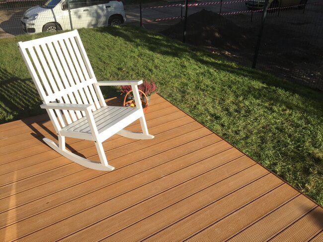 White rocking chair on a ground-level backyard deck, which can be leveled using adjustable pedestals.