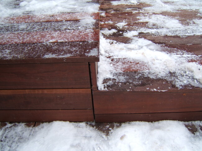 A multi-level wooden terrace deck with step edges partially covered in snow during winter weather.