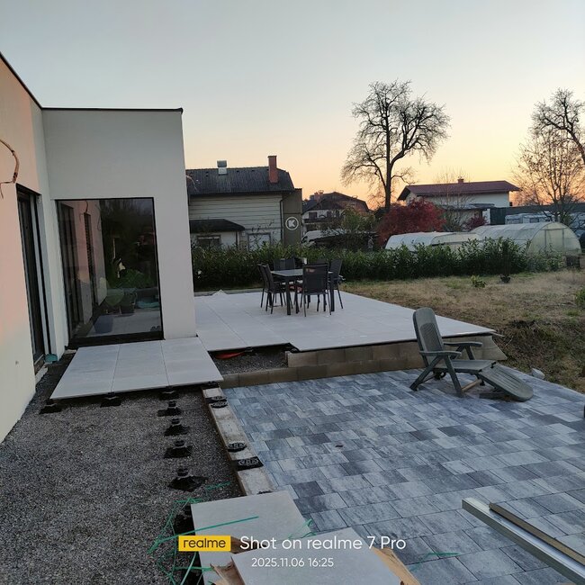 Nowoczesna instalacja patio pokazująca podniesione płyty tarasowe zamontowane na regulowanych wspornikach obok brukowanej kostką sekcji.