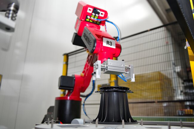 Czerwone ramię robota montujące czarny regulowany wspornik tarasowy w zautomatyzowanej fabryce.