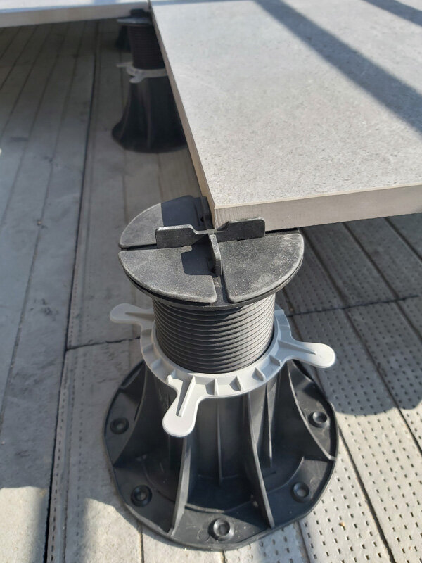 Adjustable plastic pedestal support holding up a paving slab for raised floor installation.