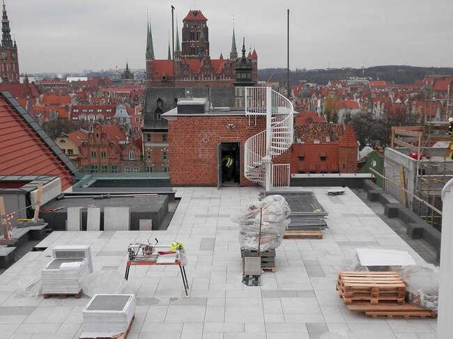 Taras na dachu w trakcie budowy z podniesioną nawierzchnią z płyt tarasowych na regulowanych wspornikach.