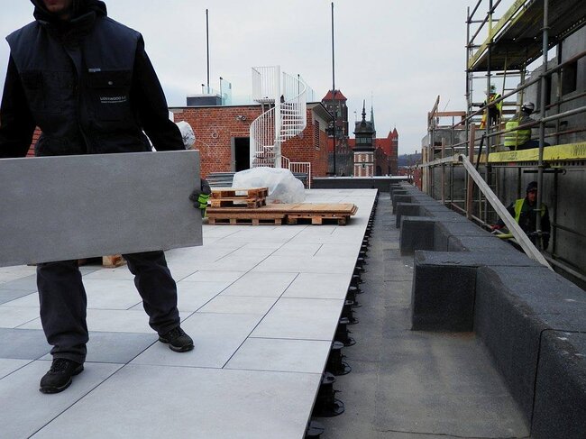 Paving tile installation using black adjustable pedestals on flat roof deck.