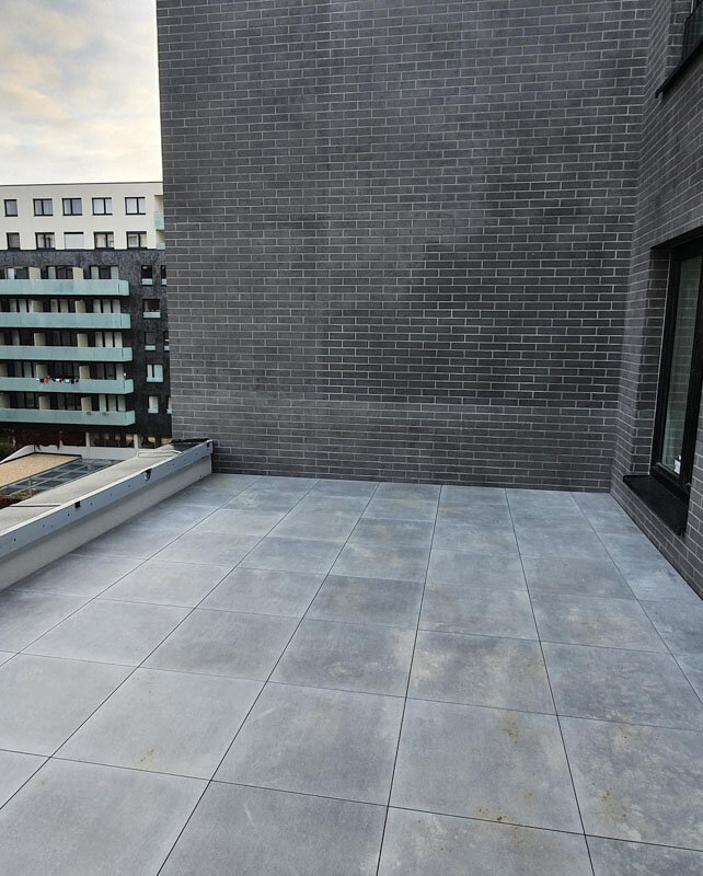 Raised outdoor terrace featuring grey porcelain pavers installed on an adjustable pedestal system next to a brick wall.