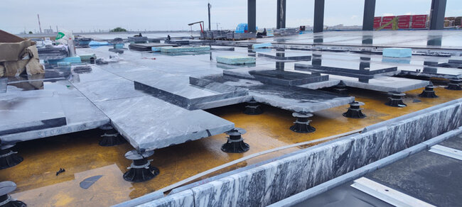 Large-scale rooftop installation of heavy natural stone pavers supported by heavy-duty adjustable pedestals.