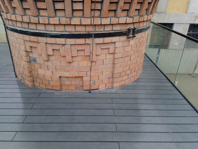 Grey composite decking installed on an adjustable pedestal system around a historic brick structure on a terrace.