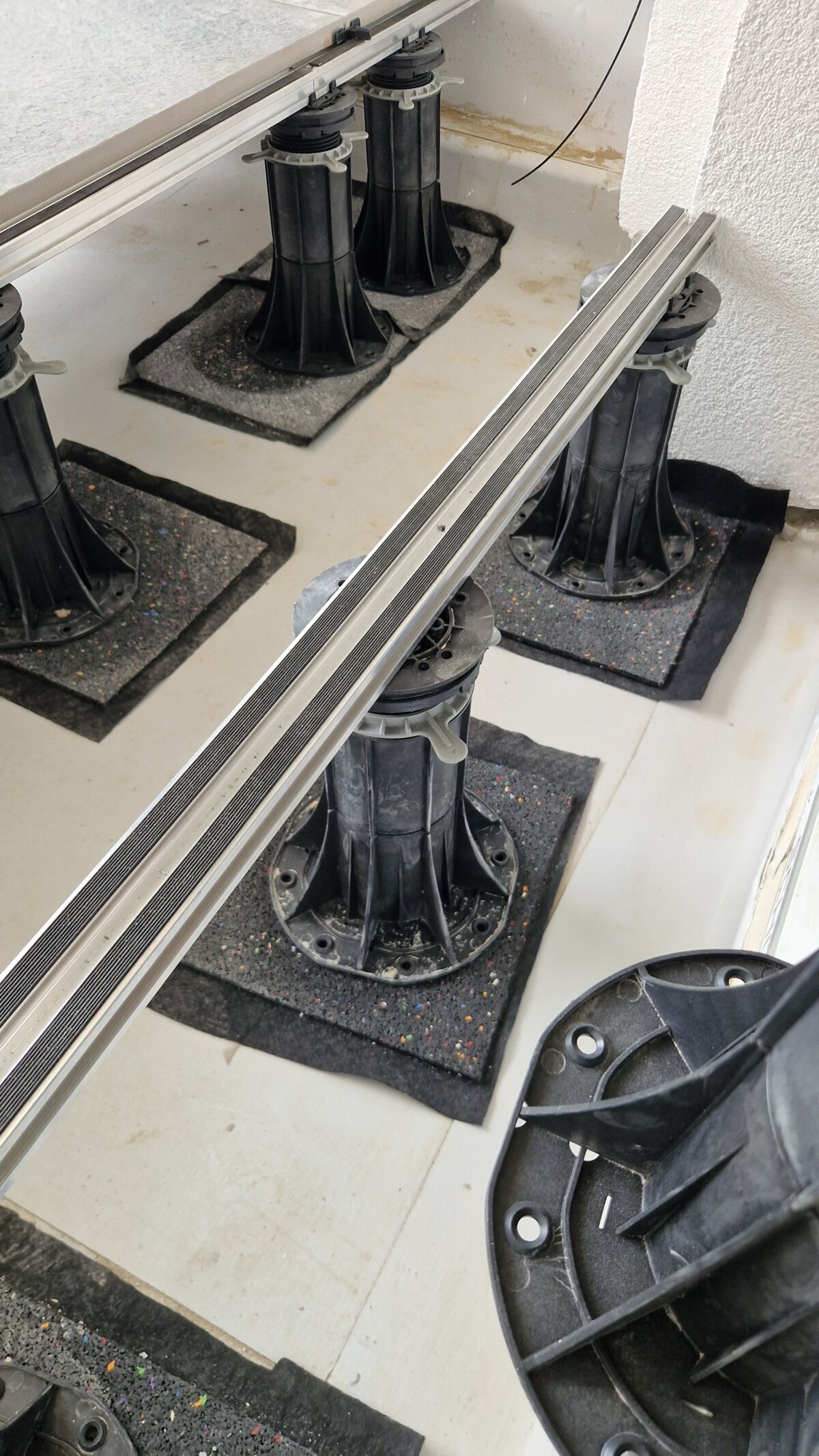 Regulowane wsporniki na podkładkach gumowych podtrzymujące aluminiowy legar do zabudowy tarasu wentylowanego.