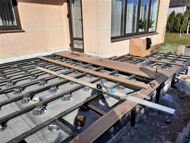Installing composite decking boards on a joist substructure supported by adjustable pedestals.