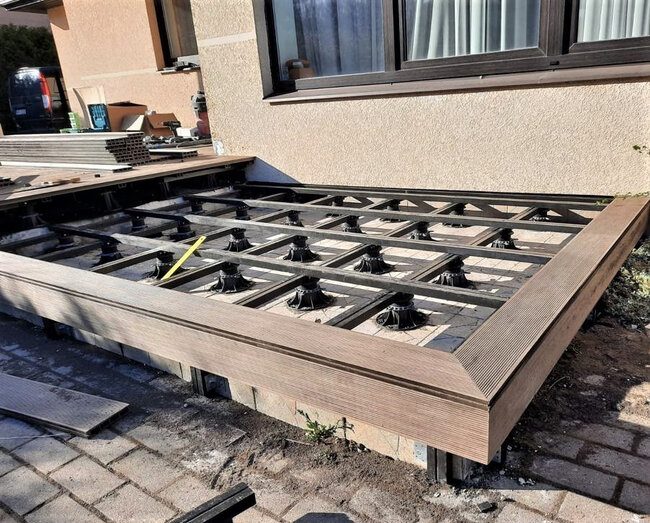 Adjustable pedestals leveling a metal joist frame with fascia board framing for composite decking installation.